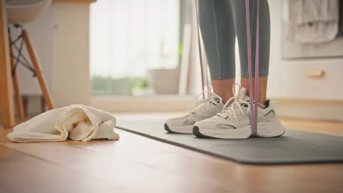 An athlete on a mat at home performs bending exercises with an elastic band Stock Footage 336669062