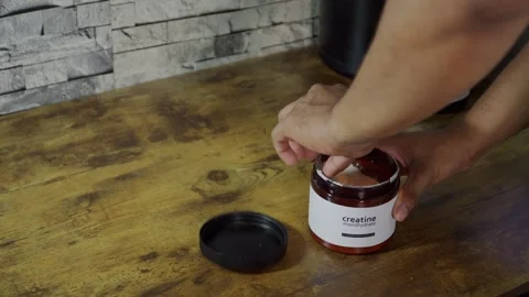 Athlete opening creatine monohydrate supplement jar and scooping powder Stock Footage 313564934