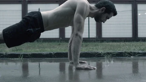 Athlete performing push-ups under the rain on the street Stock Footage 127436157