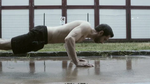 Athlete performing push-ups under the rain on the street Stock Footage 127438644