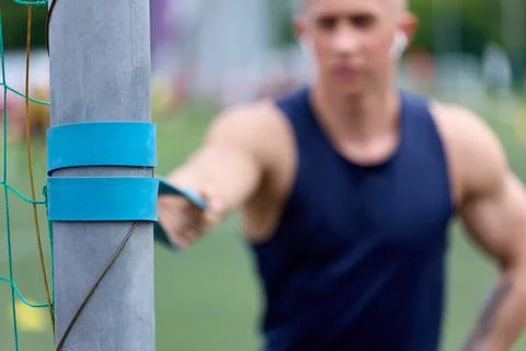 Athlete performs an exercise with an elastic band tied to bar of football goal Stock Photos