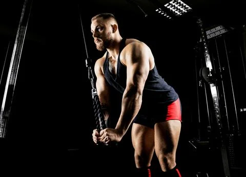 The athlete performs an exercise on the triceps on a special device Stock Photos