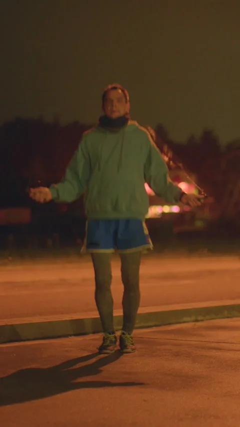 Athlete performs rapid jump rope routine beneath amber streetlamp at night Stock Footage 324592796