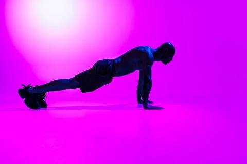 Athlete in plank position does push-ups and arm exercises on studio background Stock Photos