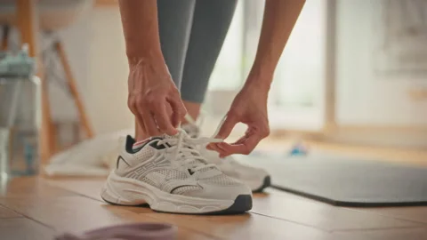 An athlete prepares for training by tying her sneakers at home during the da Stock Footage 337938422