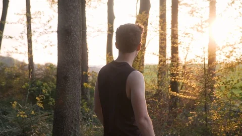 Athlete stops running in forest, puts hand in his hips and looks at sunset Stock Footage 129615494