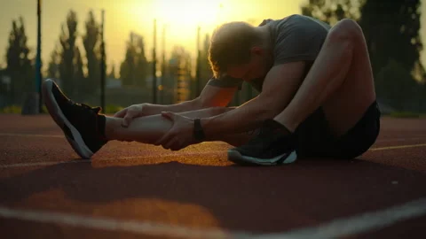 Athlete stretching on a track during sunset in an outdoor sports facility in Stock Footage 323727806