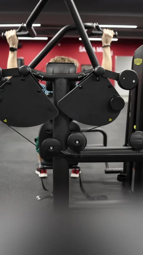 Athlete trains back strength with controlled pullups on machine Stock Footage 339321490