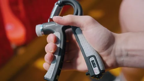 Athlete uses an hand expander. Guy trains sitting at stadium Vídeos de archivo 260829560