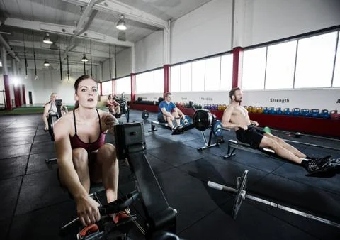 Athlete Using Rowing Machine With Friends In Fitness Center 写真素材