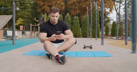 An athlete utilizes their smartphone while engaging in a workout session at an Video stock 318074269