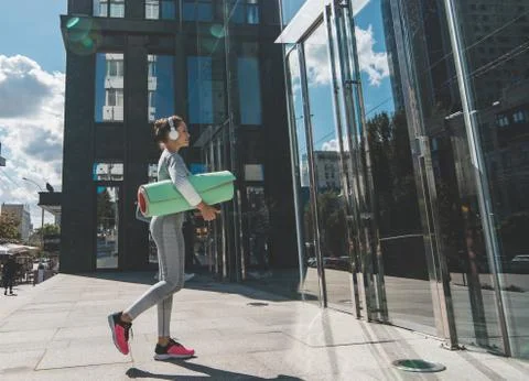An athlete in white headphones with a green mat comes to the entrance to the Stock Photos