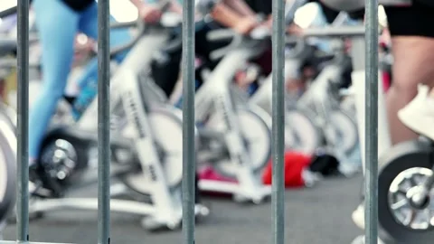 Athletes pedaling on exercise bikes during sports day behind a fence Stock Footage 317332424
