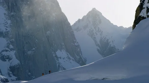 Athletes walking on snowy hill surrounded with mountains and sun beams, Alaska Stock Footage 129126539