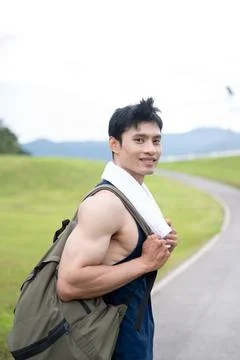 Athletic Asian man carrying a backpack and walking along the road after exe.. Stock Photos