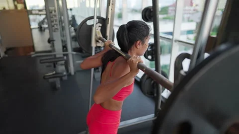 Athletic asian woman squats using barbell on smith machine at gym Stock Footage 296572679