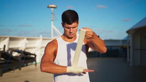 Athletic attractive man puts on hands wraps to do box outside onboard cruise Stock Footage 194440246