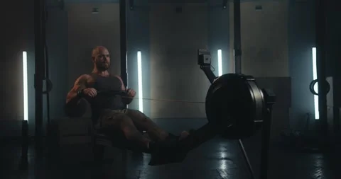 Athletic bearded man in a tank top exercising on a rowing machine in a Stock Footage 313357800