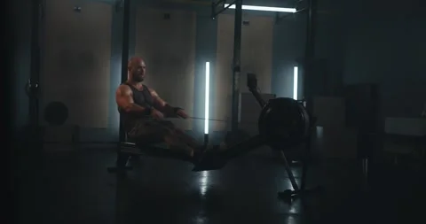 Athletic bearded man in a tank top exercising on a rowing machine in a Stock Footage 313357990
