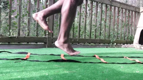 Athletic Black Man Performs Single Leg Hop Agility Ladder Drill on Turf, Slow Stock Footage 161425117