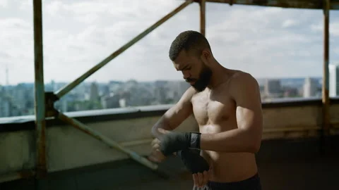 Athletic Black man preparing for boxing by wrapping hands on an empty rooftop Stock Footage 328715804