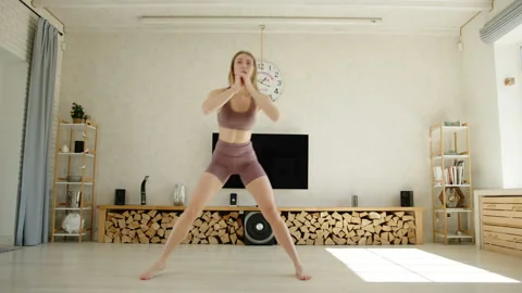 Athletic blonde performs side lunges with lifting leg to chest. Home workout Stock Footage 242109391