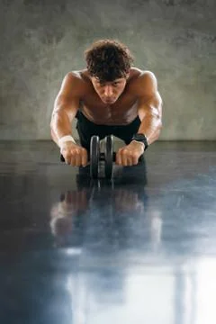 Athletic bodybuilder workout with toning wheel in gym and fitness club Stock Photos