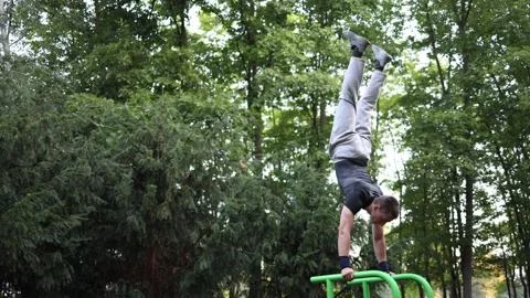 Athletic boy balances in perfect handstand on green bars at outdoor gym surround Stock Footage 316701716