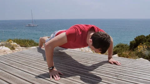 Athletic Caucasian man performs pushups on rocky coast beach on sunny day Stock Footage 64955582