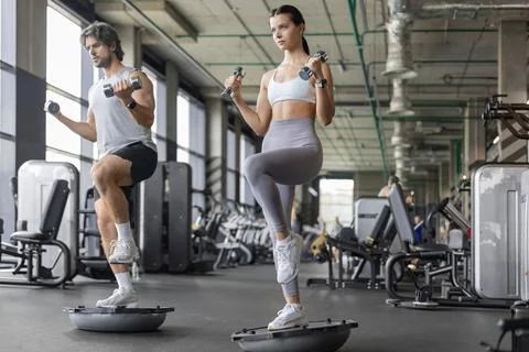 Athletic couple doing single-leg balance exercise on BOSU ball at gym 库存照片