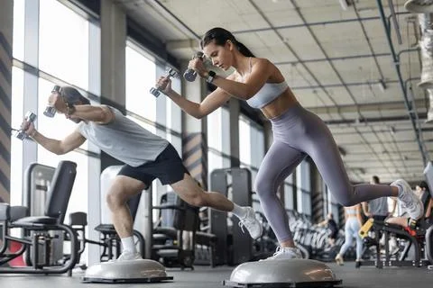 Athletic couple doing single-leg balance exercise on BOSU ball at gym Stock Photos