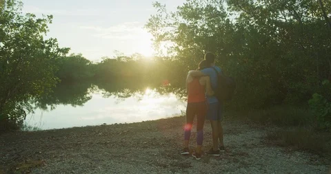 Athletic couple watching the sunset over a lake in a forrest Stock Footage 104229737