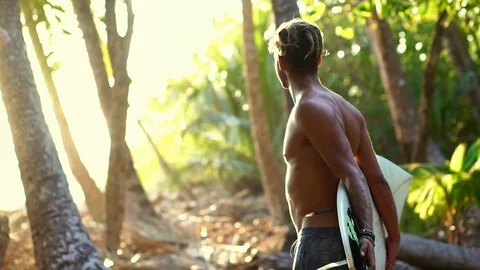 Athletic fit guy on beach, holding surfboard during sunset Stock Footage 108568729