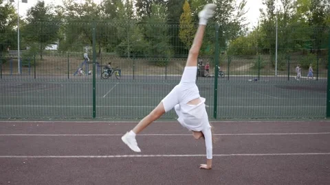 Athletic girl doing an acrobatic flip on one arm. A sporty child exercises at th Stock Footage 292746708