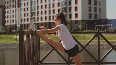 Athletic girl doing a leg stretch on the pier on the shore of pond. Stock Footage 154846680