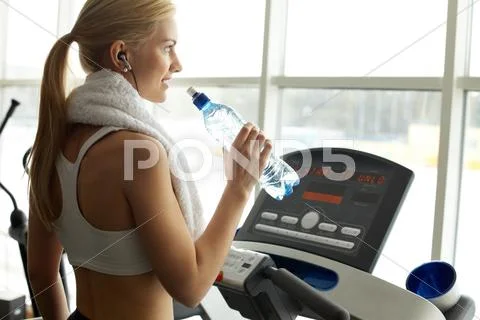 An athletic girl in gym drinking water and looking at window Stock Photos