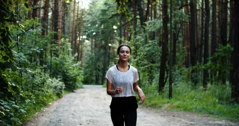 Athletic girl running in the Park and doing exercises Jogging while listening to Stock Footage 202279341