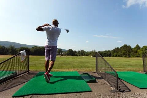 Athletic golfer swinging at the driving range dressed in casual attire. Stock Photos