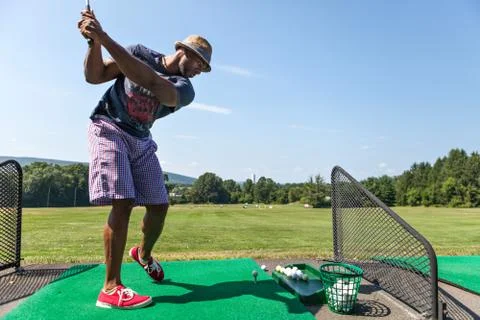 Athletic golfer swinging at the driving range dressed in casual attire. Stock Photos
