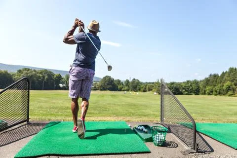 Athletic golfer swinging at the driving range dressed in casual attire. Stock Photos