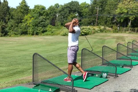 Athletic golfer swinging at the driving range dressed in casual attire. Stock Photos