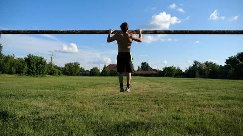 Athletic guy doing pull ups on football goal crossbar at stadium. Young mus.. Stock Photos