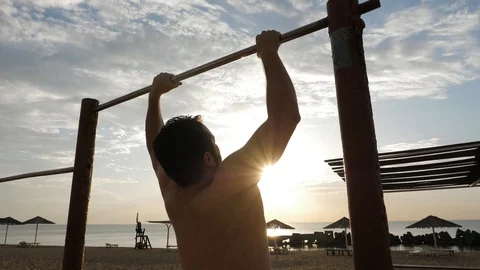 Athletic guy exercises pull-ups on sand beach slow motion Stock Footage 124024499
