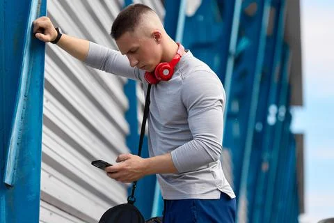 Athletic guy with hand leaned on iron support of stadium, answers the phone Stock Photos
