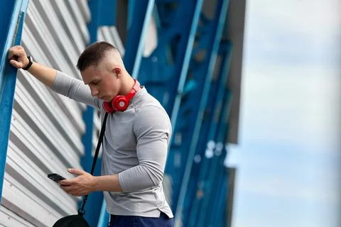 Athletic guy with hand leaned on iron support of stadium, answers the phone Stock Photos