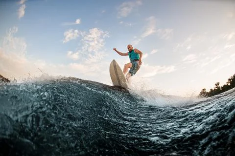 Athletic guy having fun and wakesurfing on the board down the river Stock Photos