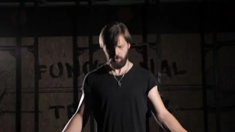 Athletic guy some jump rope exercises in dark room under light. Video stock 142225932