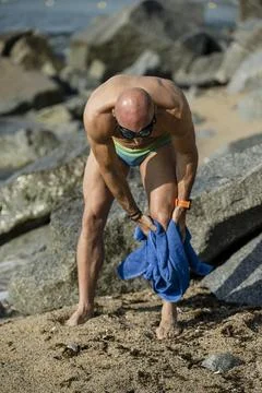 Athletic guy toweling off his legs with swim glasses in a beach with rocks. Fit Stock Photos