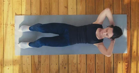 Athletic lady does crunches lying on mat on wooden floor Stock Footage 153510870