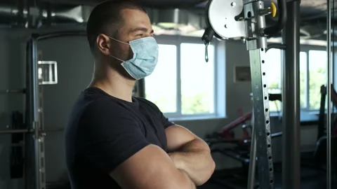 Athletic man with big biceps standing in the gym in a mask in a male with his Stock Footage 134909324